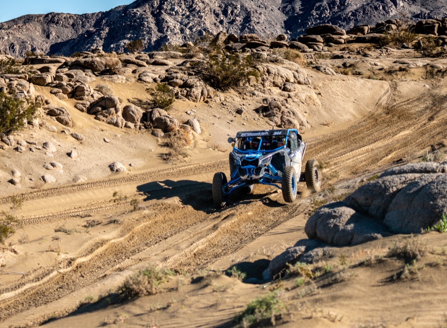 Side-by-side buggy winding along a sunlit gravel trail between rock outcrops